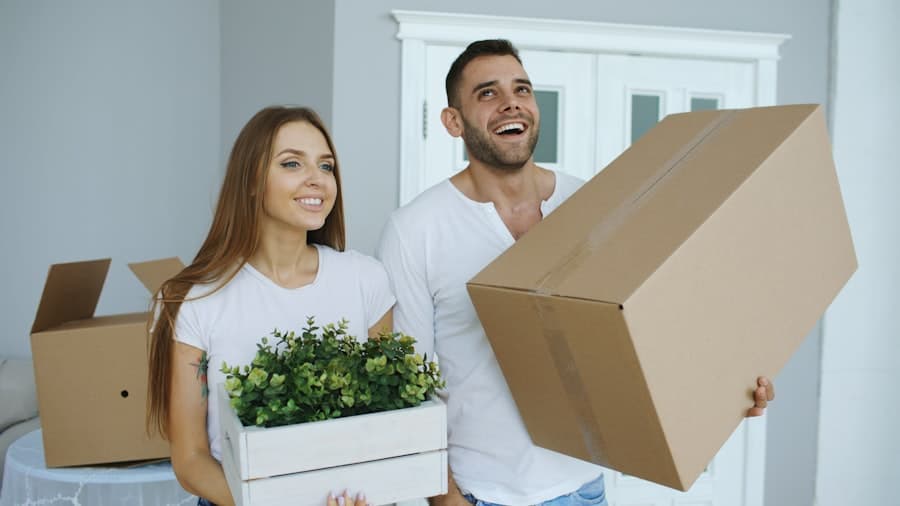 Couple carrying moving boxes and a plant into their new home